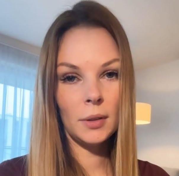 Małgorzata Tomaszewska podczas prezentacji programu telewizyjnego, z mikrofonem, w dynamicznej pozie, na tle studia.