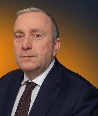 Grzegorz Schetyna – uśmiechnięty portret w tle parlamentu.