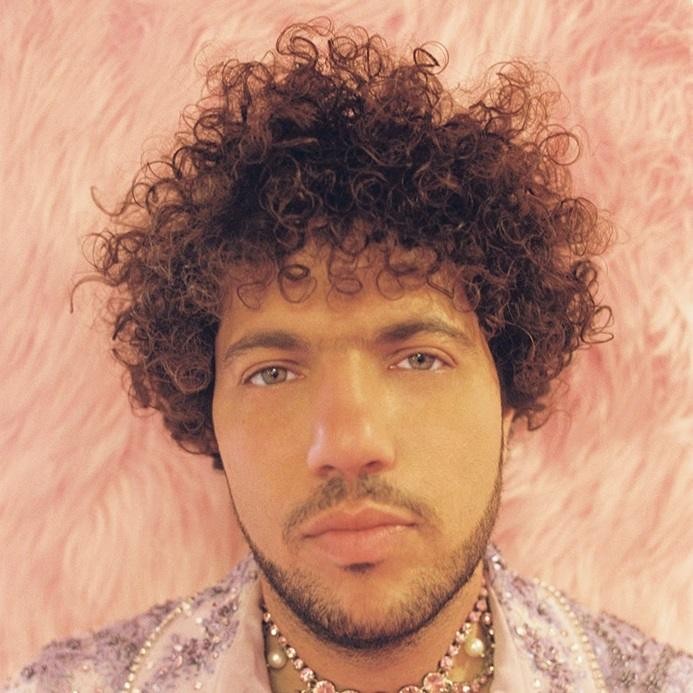 Benny Blanco skupiony przy konsoli mikserskiej w studiu nagraniowym, otoczony sprzętem, w ciepłym świetle.