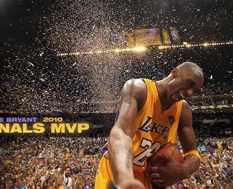 Kobe Bryant wykonujący rzut z odchylenia w stroju Lakersów, w tle rozmyty tłum areny.