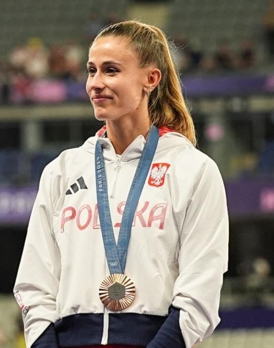 Natalia Bukowiecka, uśmiechnięta, w sportowym stroju, pozująca na tle rozmytego krajobrazu.