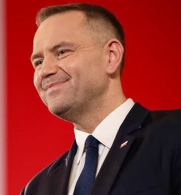 Karol Nawrocki podczas publicznego wystąpienia, angażujący się w rozmowę z widownią na tle historycznego obiektu.