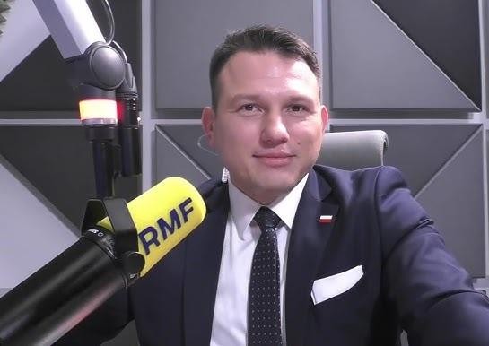 Sławomir Mentzen przemawiający na wiecu politycznym, dynamicznie gestykulujący, otoczony rozmazanym tłumem.