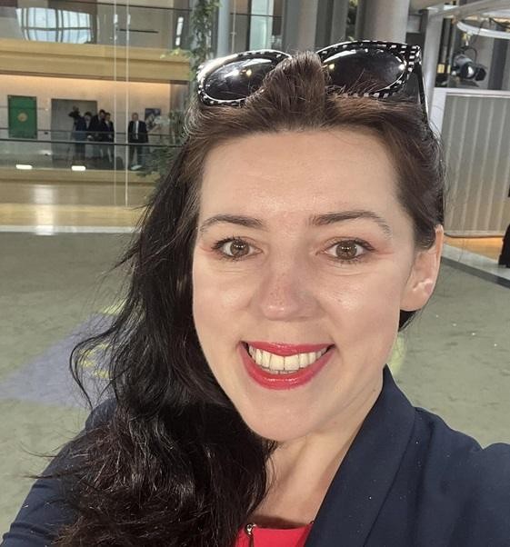 Dominika Ćosić przeglądająca Instagram na smartfonie, w tle europejskie miasto.