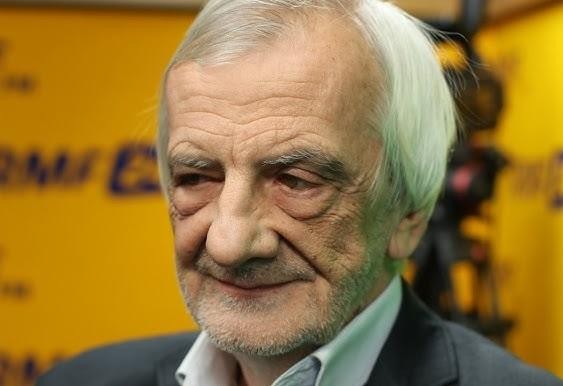 Ryszard Terlecki podczas wystąpienia publicznego, z gestykulacją, w tle zamazane wnętrze sali sejmowej.