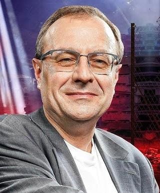 Antoni Dudek w studiu telewizyjnym, dynamicznie komentujący wydarzenia historyczne i polityczne.