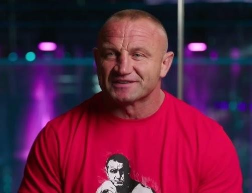 Zbliżenie na twarz Mariusza Pudzianowskiego, ukazujące jego zdeterminowany i skupiony wyraz, z tłem sugerującym trening lub walkę.