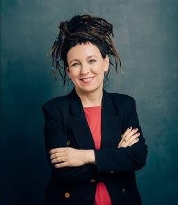 Olga Tokarczuk podczas czytania książki, z wyrazistą mimiką, trzymająca w ręku powieść