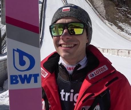 Jakub Wolny trenujący na skoczni narciarskiej w Wilkowicach, z widokiem na okoliczny krajobraz.